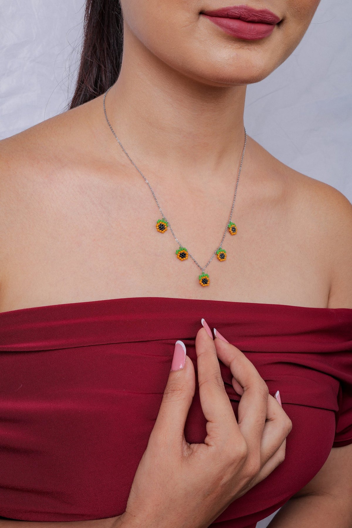 Model wearing silver chain necklace with five orange, black and green pixel-beaded charms