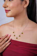 Side view of silver charm necklace with orange beaded charms with black centres and green tops