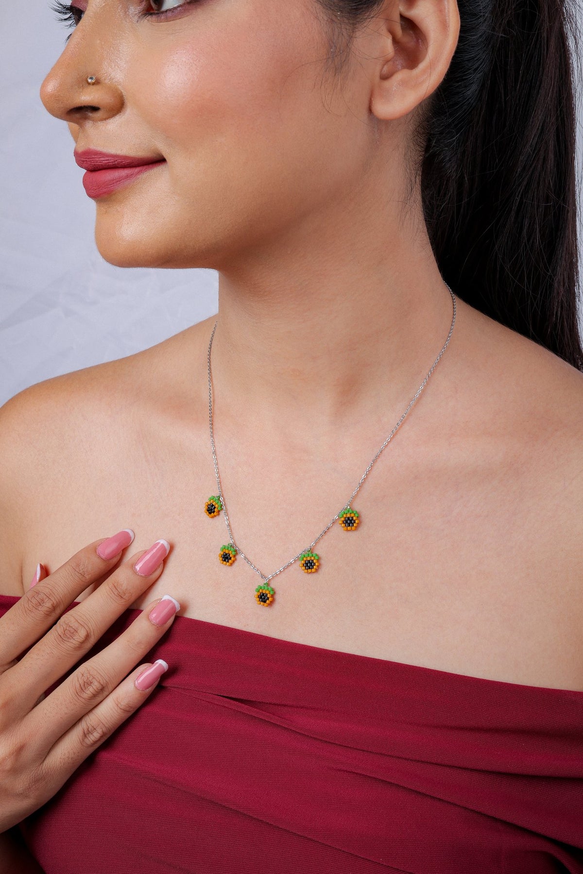 Side view of silver charm necklace with orange beaded charms with black centres and green tops