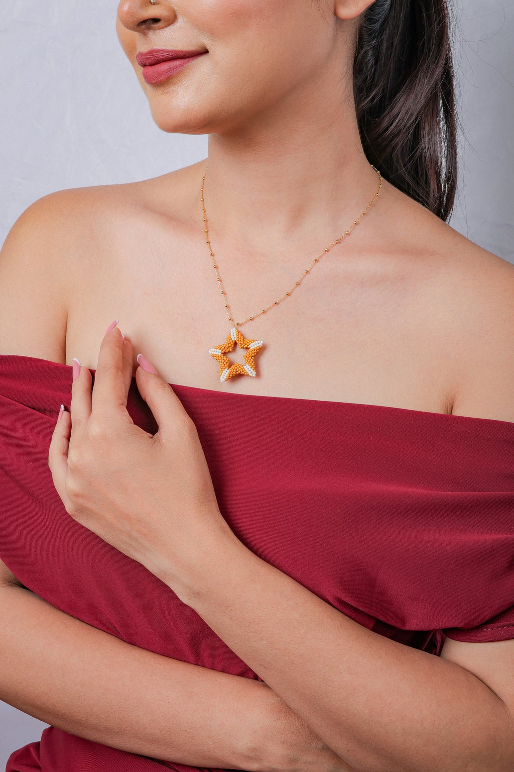 Orange star pendant necklace worn with a red off-shoulder top, hand at the shoulder