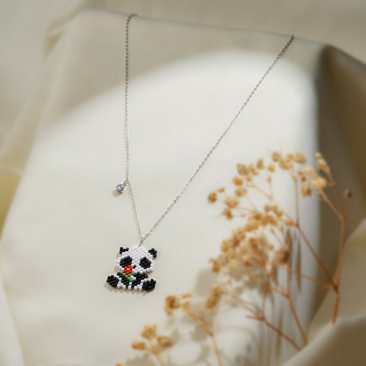 Beaded black and white panda pendant holding a red flower on a silver-tone chain