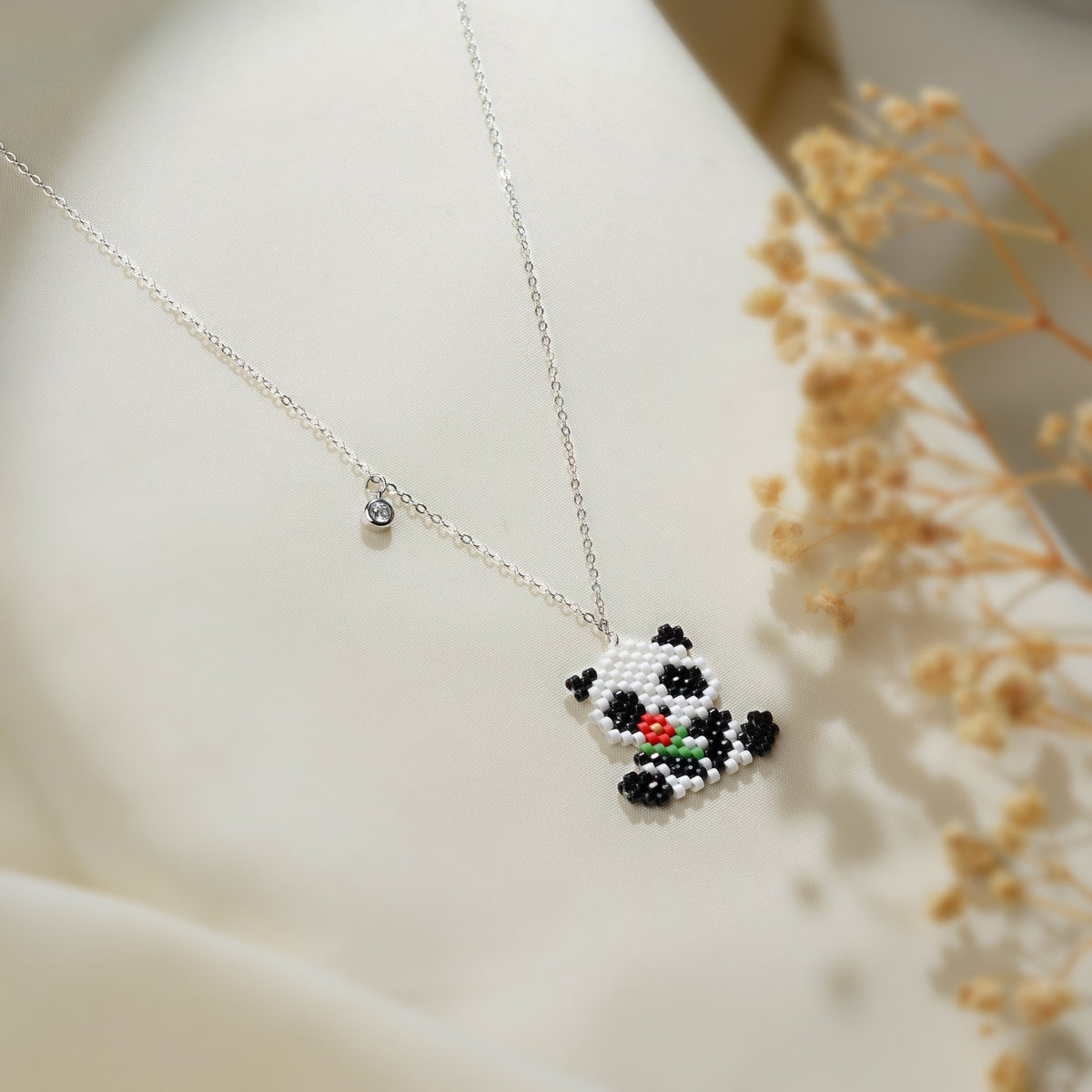 Panda pendant with red flower and crystal charm on a silver-tone chain beside dried flowers