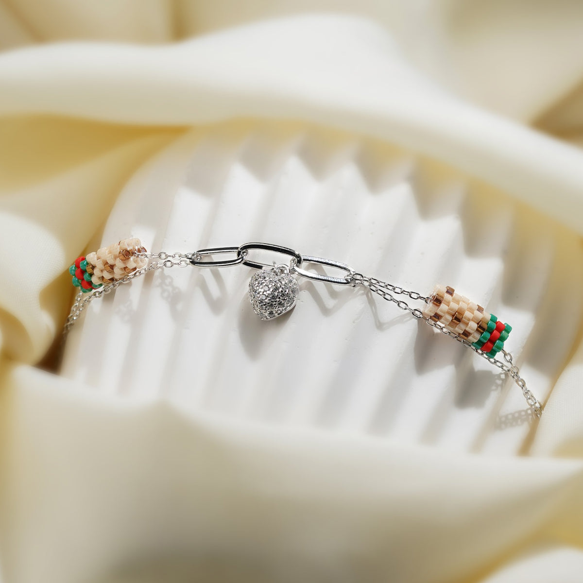 Silver paperclip heart charm bracelet draped over a white fluted stand