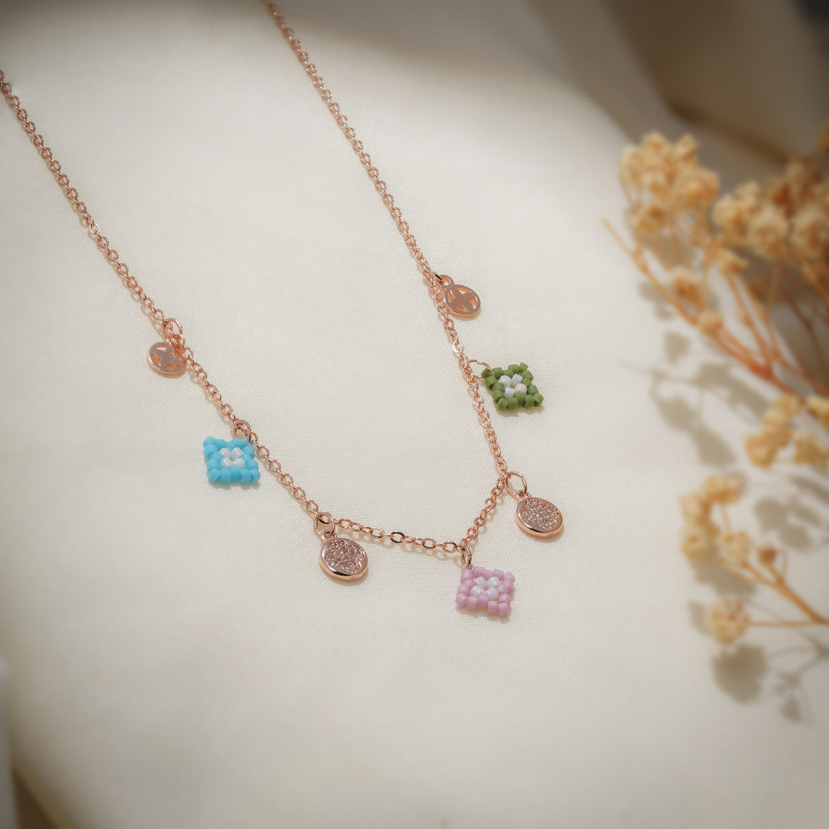Close-up of turquoise, pink and olive-green beaded charms between crystal-pavé discs on rose-gold chain