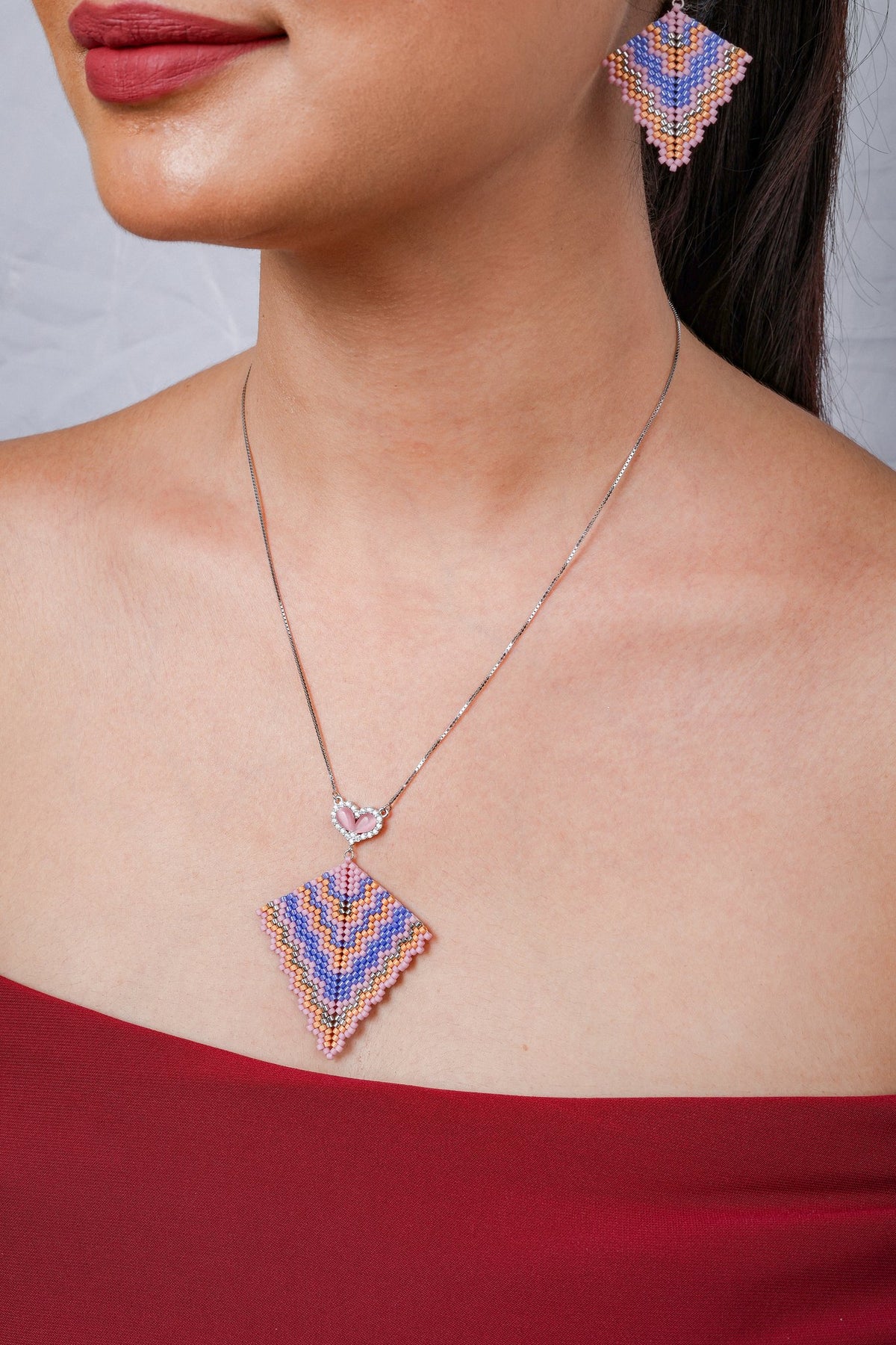 Close view of chevron-beaded kite pendant below a pink crystal-edged heart on a silver chain