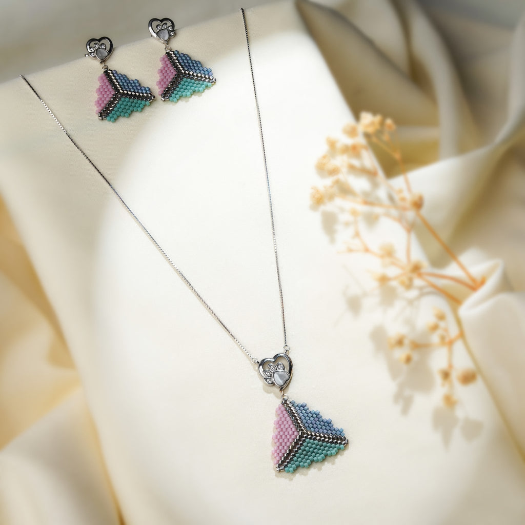 Pastel pyramid necklace set with heart paw-print studs laid on cream fabric