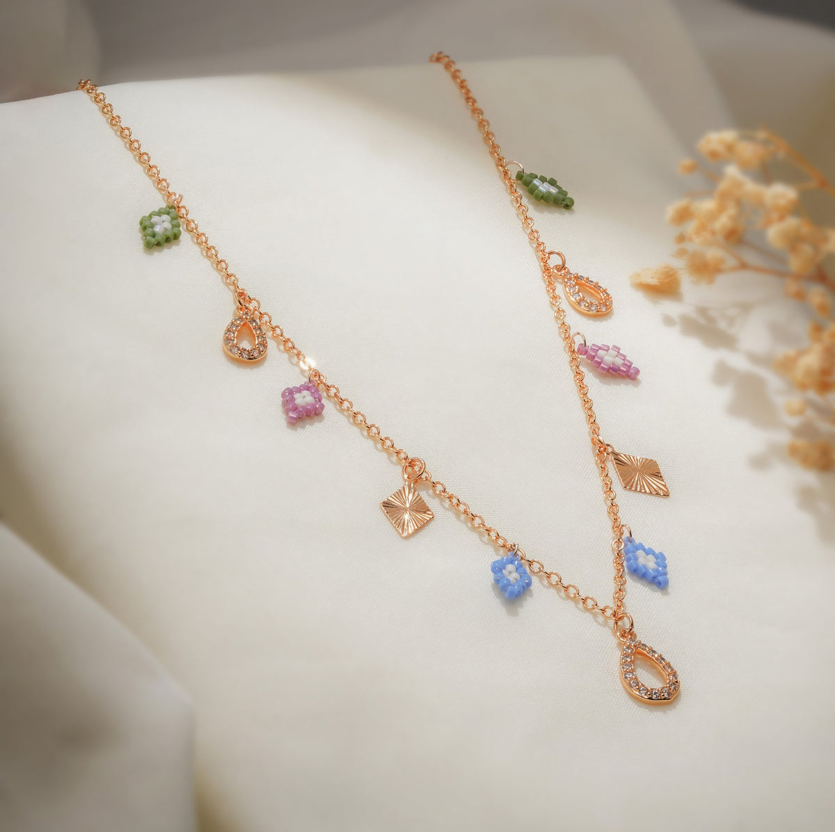 Rose-gold charm necklace with blue, pink and green beaded rhombus charms and crystal teardrops on cream silk
