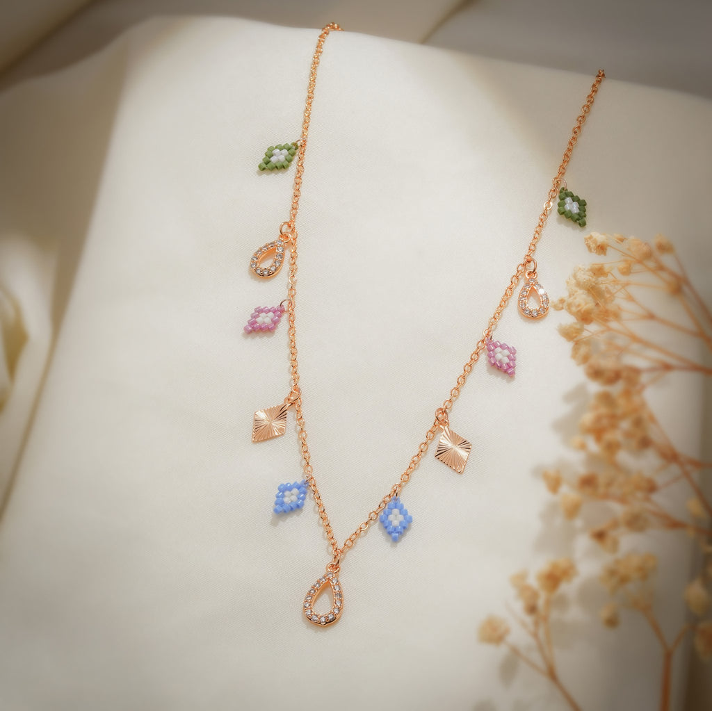 Angled view of pastel beaded rhombus, sunburst rhombus and crystal teardrop charms on rose-gold chain