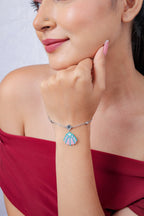 Model resting chin on hand wearing silver bracelet with pink and turquoise seashell charm