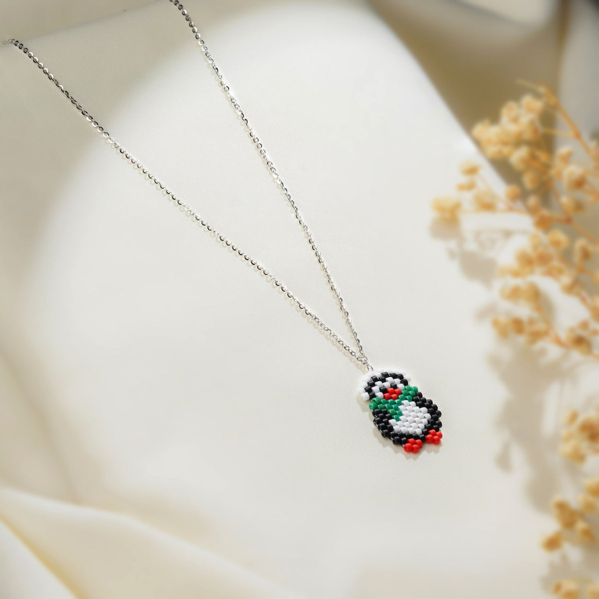 Silver chain necklace with a beaded black and white penguin pendant wearing a green scarf
