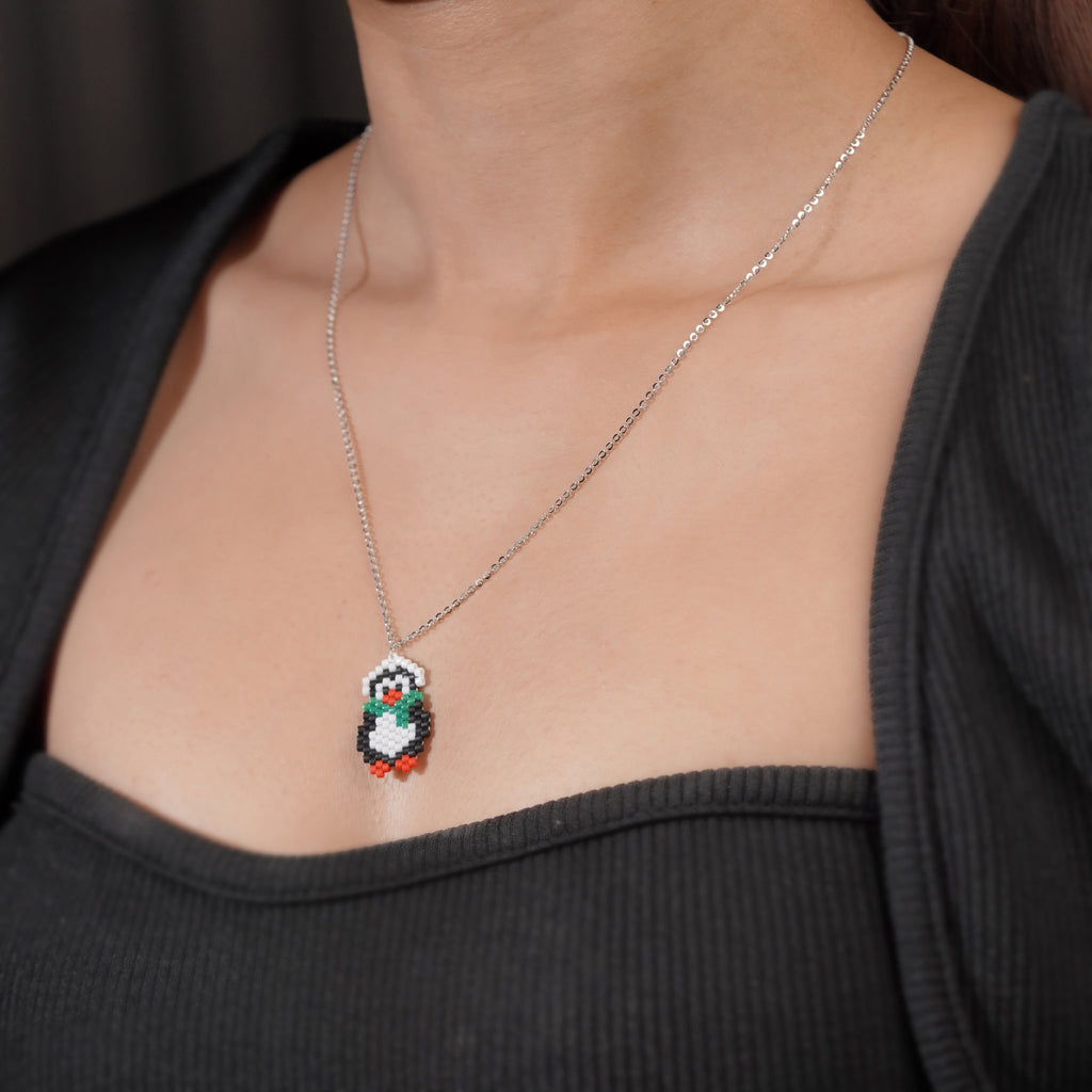 Model wearing silver necklace with beaded penguin pendant against a black top
