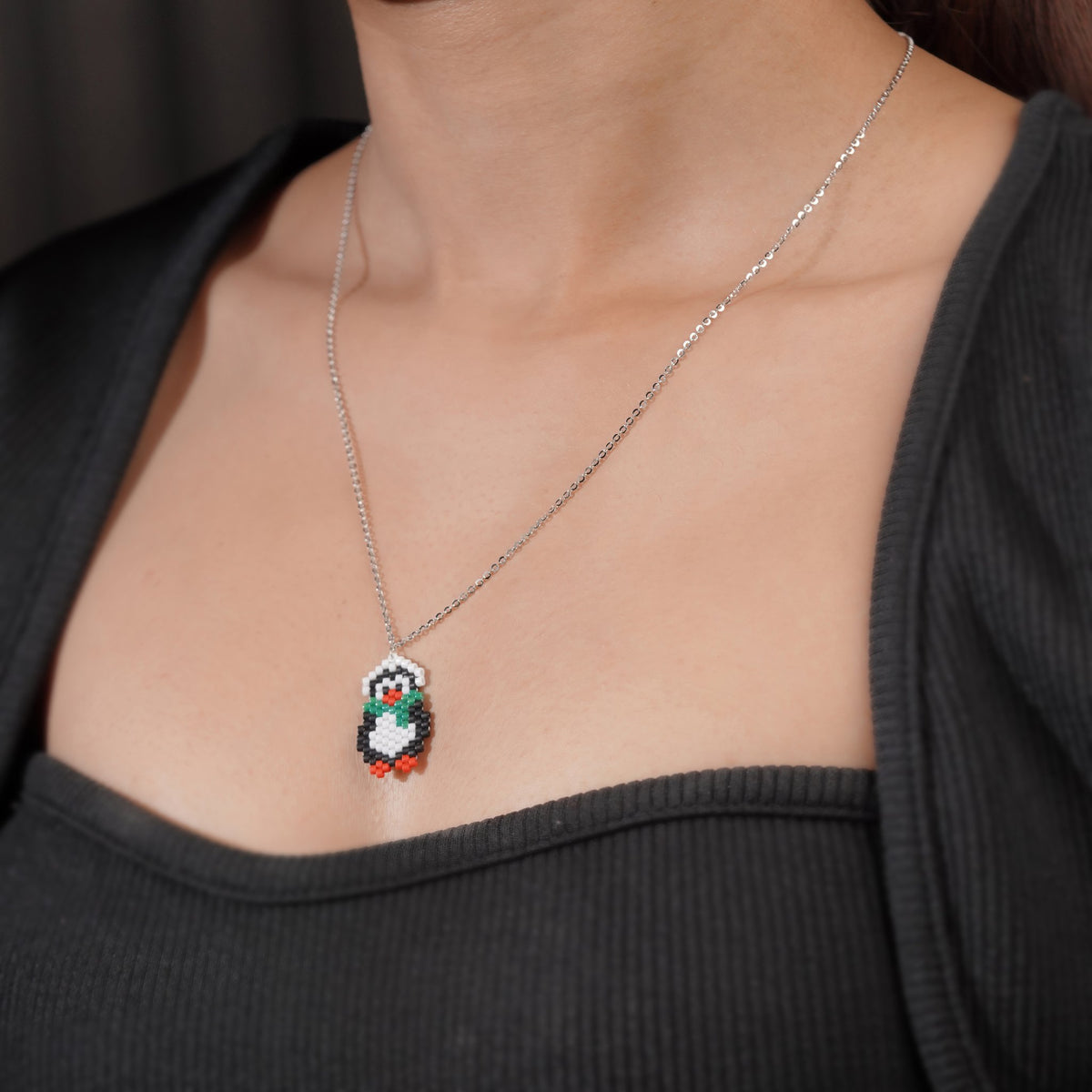 Model wearing silver necklace with beaded penguin pendant against a black top