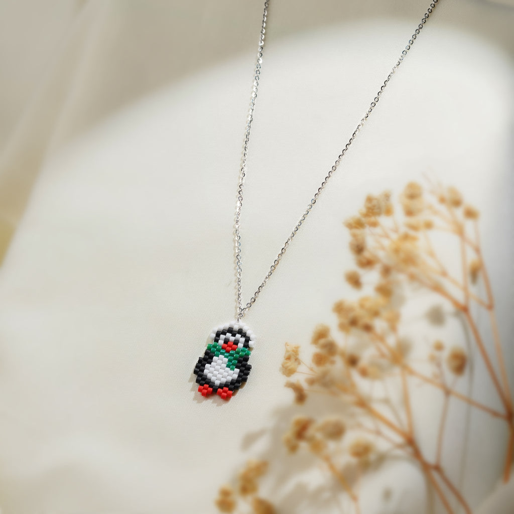 Close view of beaded penguin pendant with red beak, green scarf and red feet on silver chain