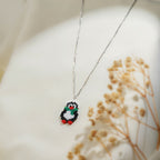 Close view of beaded penguin pendant with red beak, green scarf and red feet on silver chain