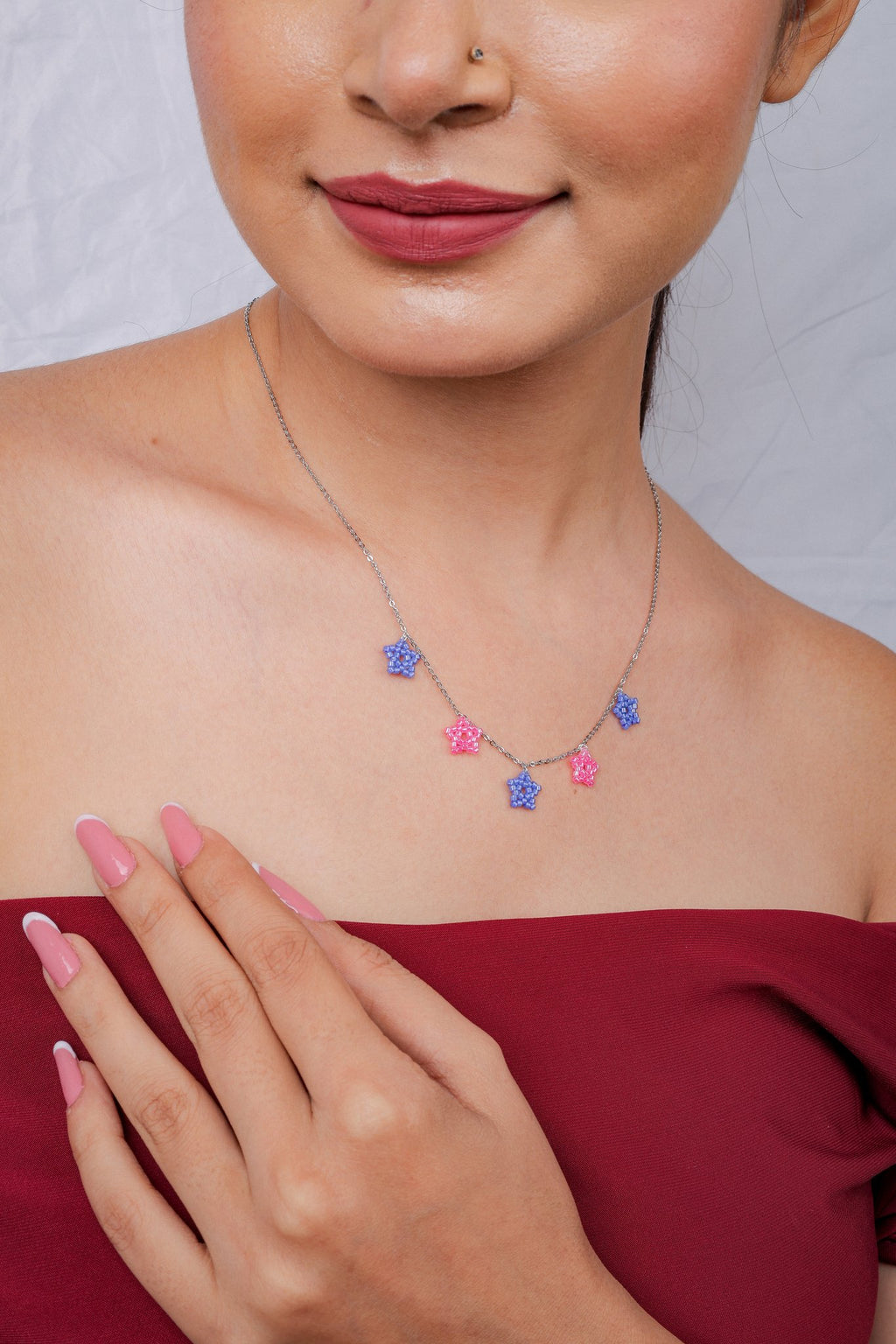 Model smiling with hand on chest, wearing dainty periwinkle and pink star necklace