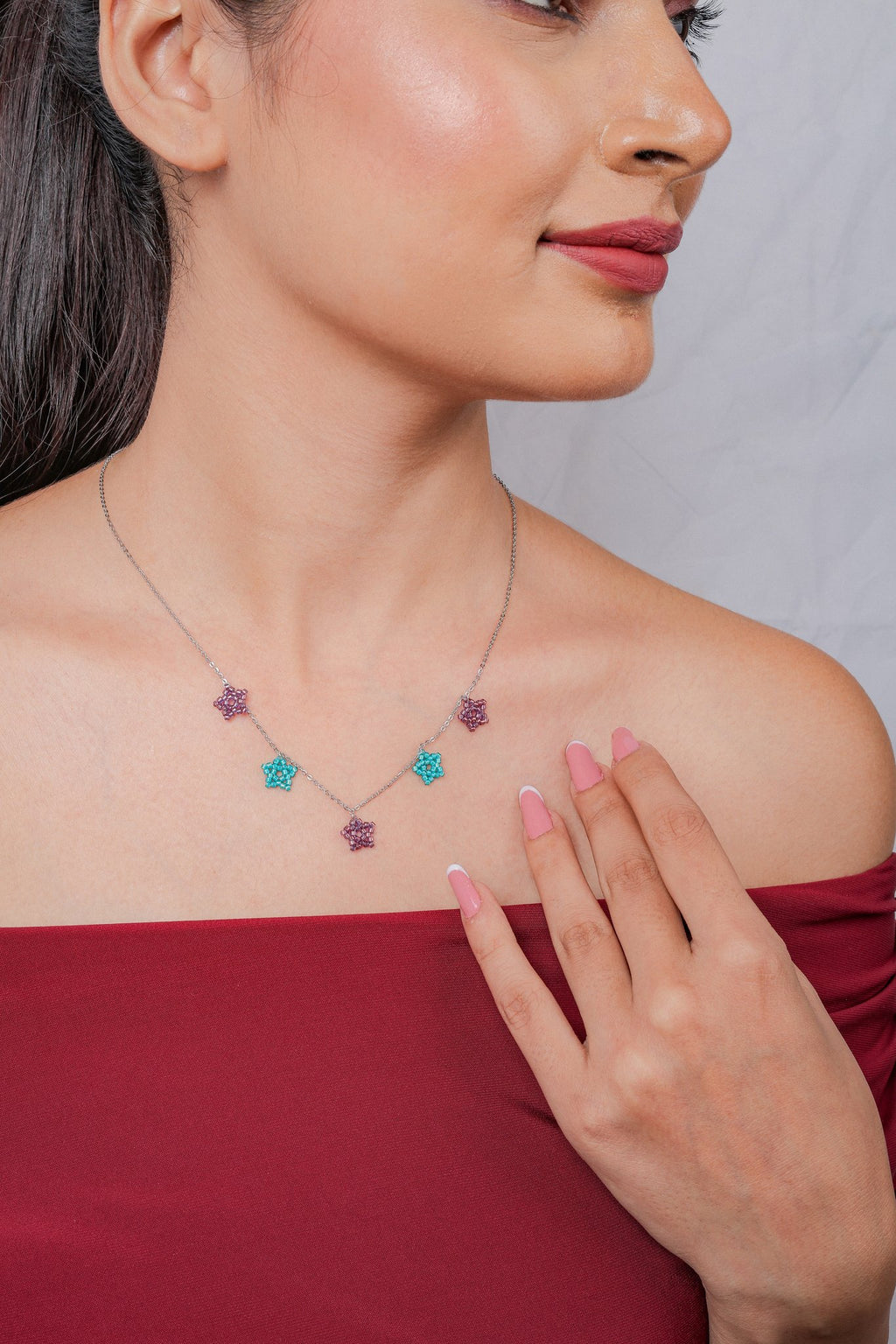 Close-up of plum and teal beaded star charms on fine silver chain at the collarbone