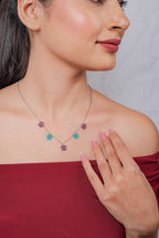 Close-up of plum and teal beaded star charms on fine silver chain at the collarbone