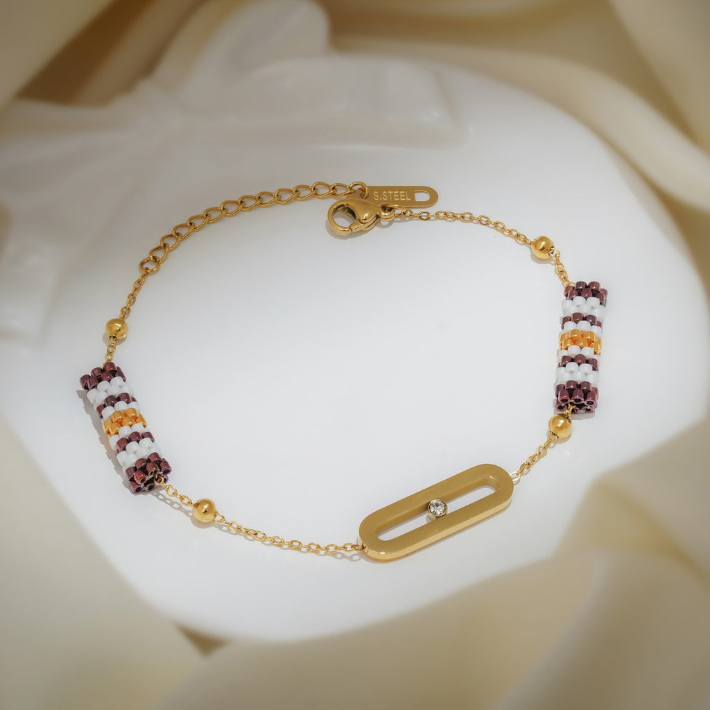 Gold chain bracelet with two plum, white and gold striped beaded barrels and an open oval link