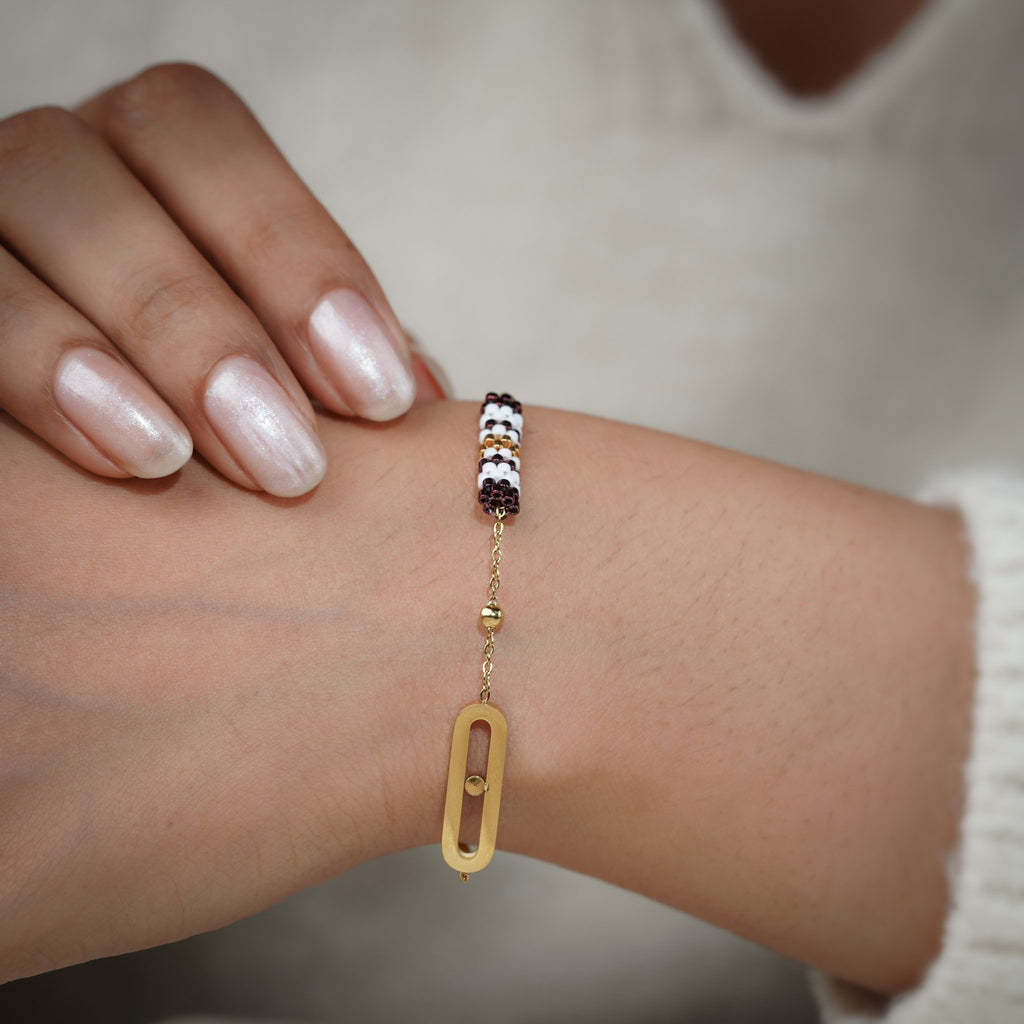 Gold charm bracelet with striped beaded barrel and oval link worn on the wrist