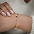 Gold charm bracelet with striped beaded barrel and oval link worn on the wrist