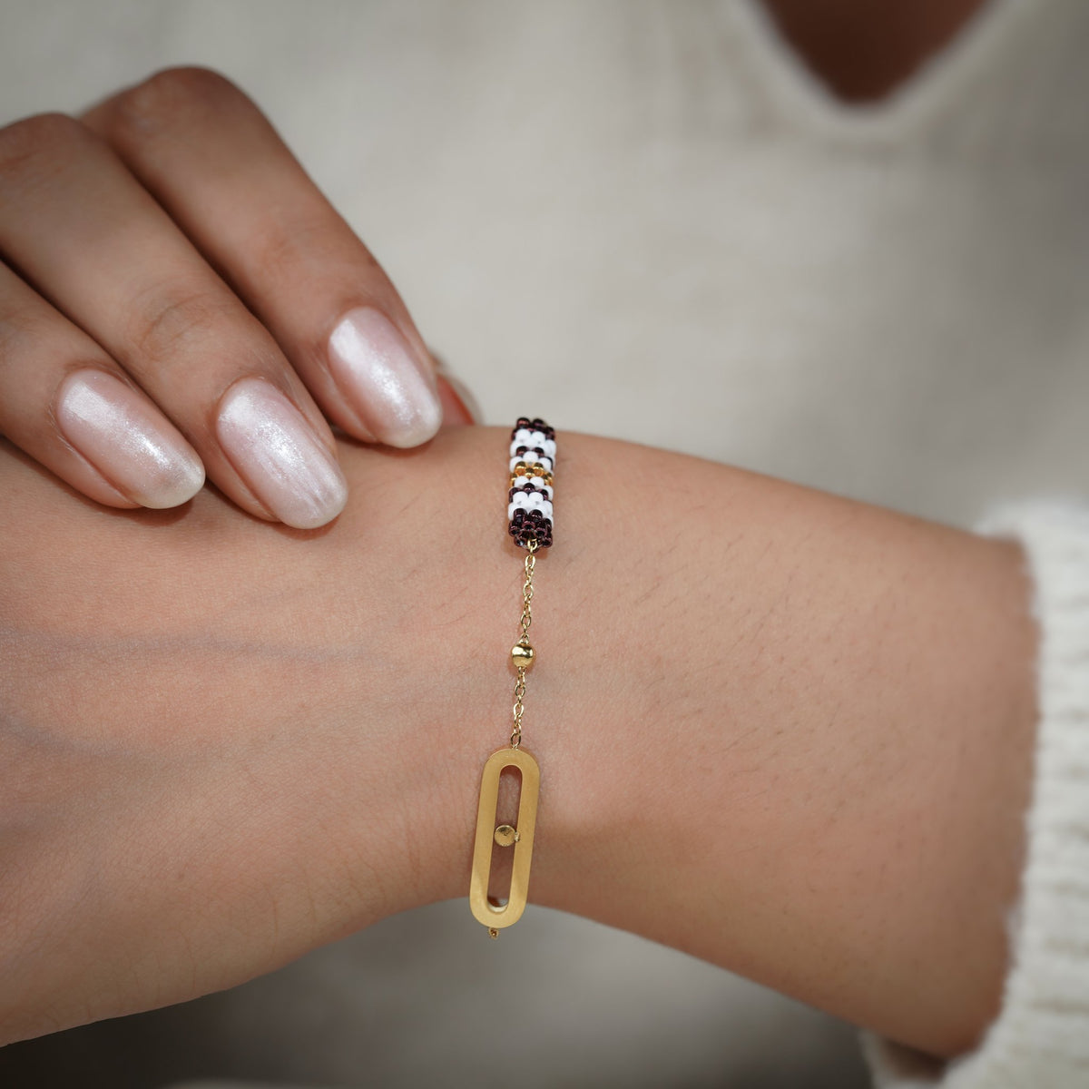 Gold charm bracelet with striped beaded barrel and oval link worn on the wrist