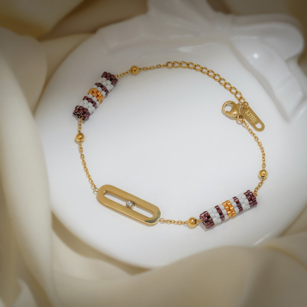 Gold bracelet with plum-striped beaded barrels, gold ball beads and oval link holding one crystal