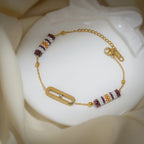 Gold bracelet with plum-striped beaded barrels, gold ball beads and oval link holding one crystal