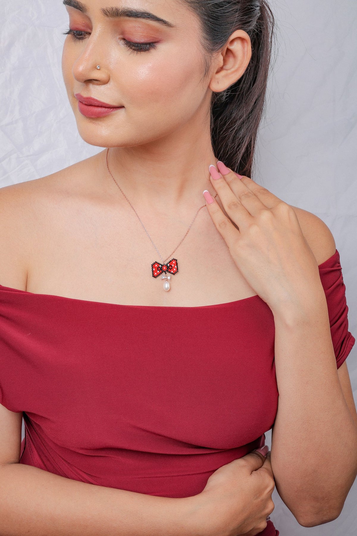 Model looking down, wearing the red and black beaded bow pendant on a fine chain