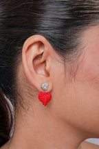Close-up of a crystal heart stud earring with a puffed red beaded heart drop