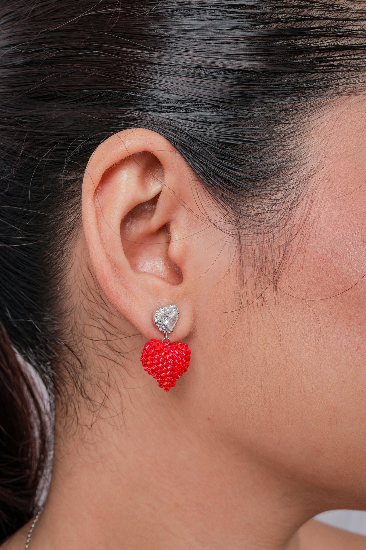 Close-up of a crystal heart stud earring with a puffed red beaded heart drop