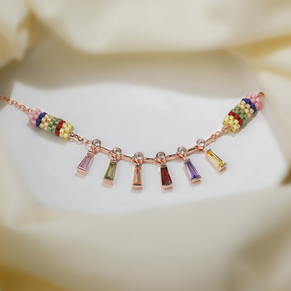 Rose-gold bracelet with six rainbow baguette crystal drops between two striped beaded barrels