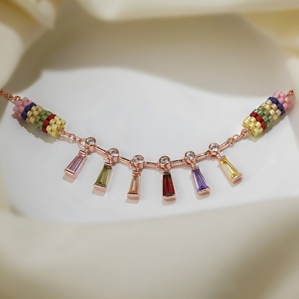 Rose-gold charm bracelet with pink, green, red, purple and yellow baguette drops on cream silk