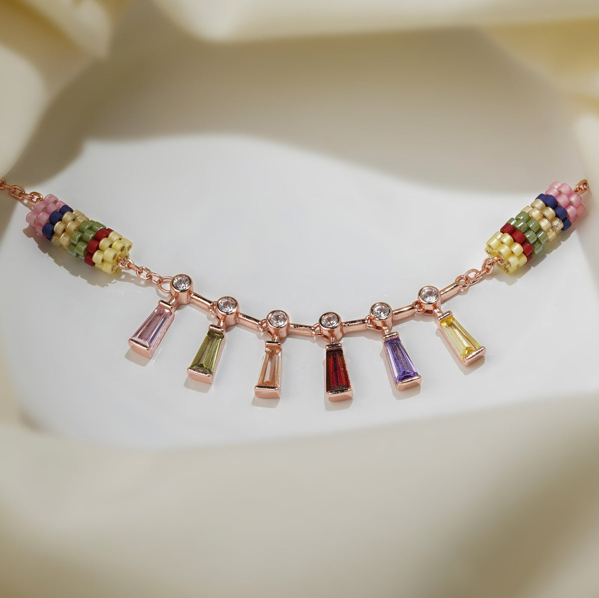 Rose-gold charm bracelet with pink, green, red, purple and yellow baguette drops on cream silk