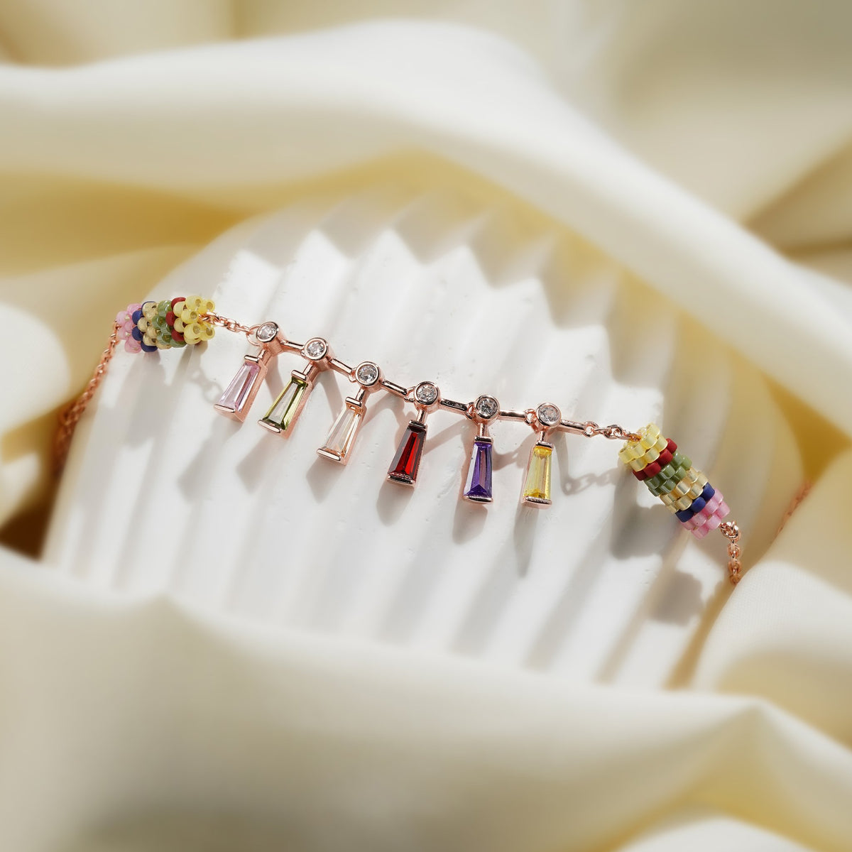 Rainbow baguette crystal bracelet with multicolour beaded barrels draped over a ribbed stand
