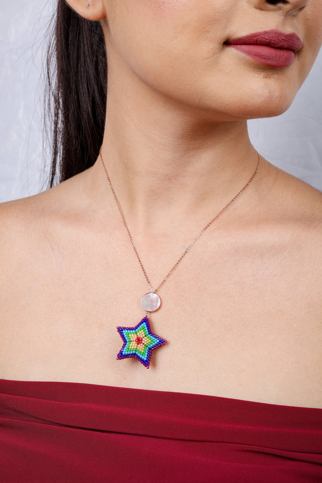 Rose-gold-tone chain with a pearly disc and a puffed rainbow beaded star pendant on a model