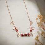 Rose-gold ball-chain necklace with red and white beaded barrels and flower-shaped charms on cream fabric