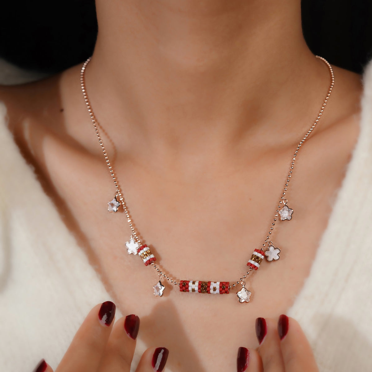 Model wearing rose-gold necklace with red beaded barrels and clear crystal flower charms