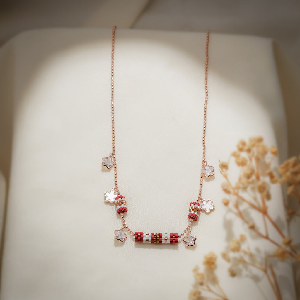 Full-length view of rose-gold charm necklace with red beaded barrels and flower charms
