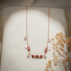 Full-length view of rose-gold charm necklace with red beaded barrels and flower charms