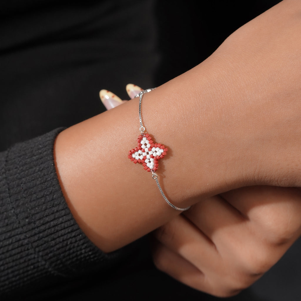 Model wearing the red beaded clover bracelet on a silver chain against a black sleeve