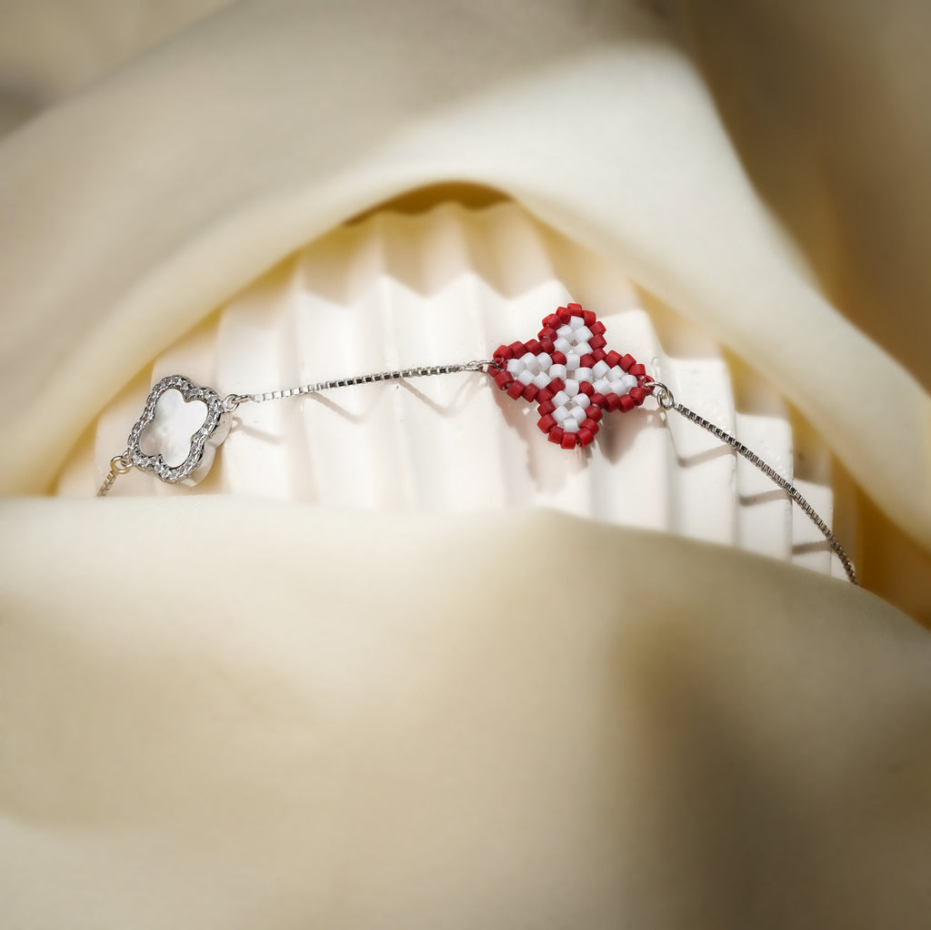 Red clover charm bracelet on a silver box chain draped over a white stand