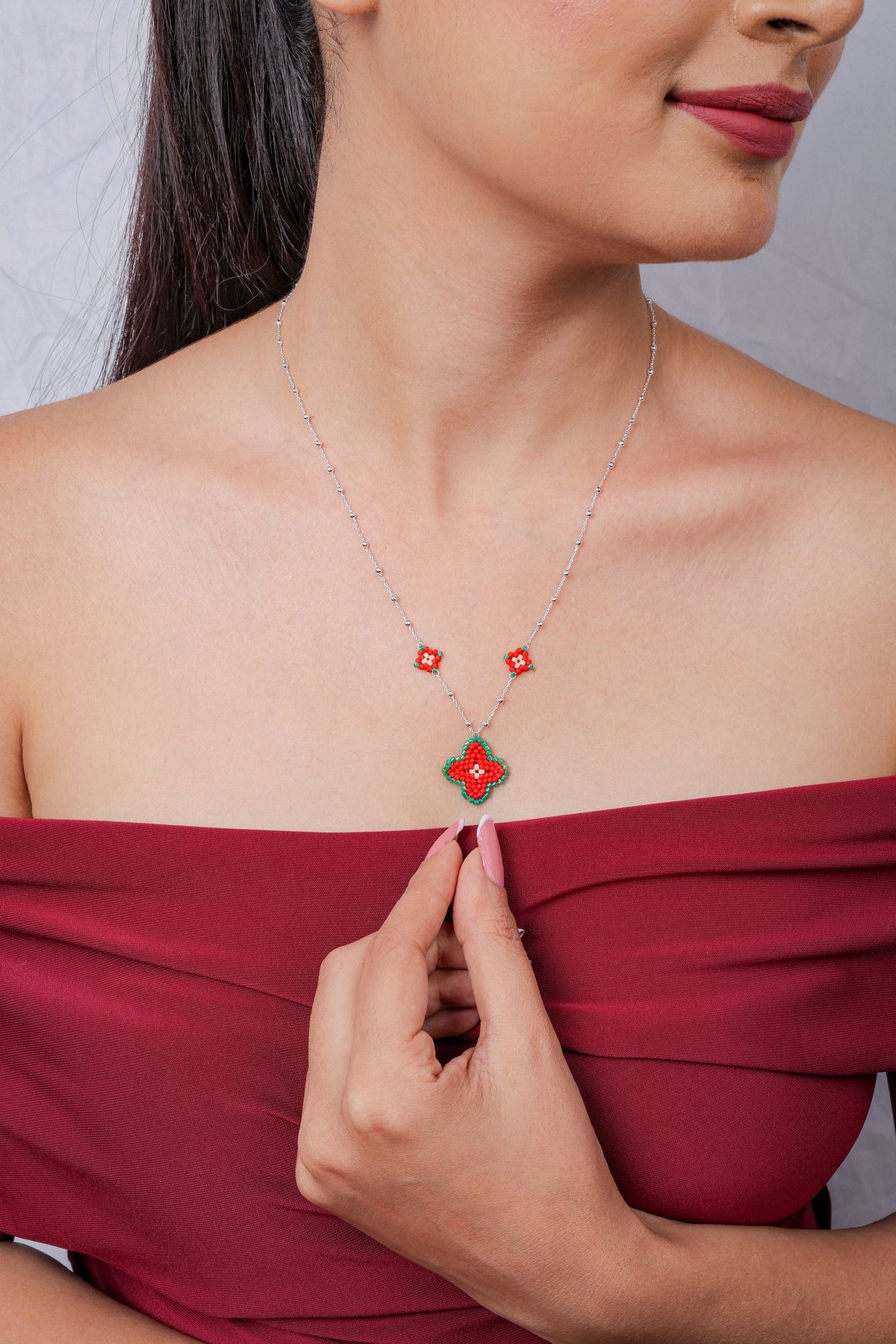 Model in red top wearing silver chain necklace with red quatrefoil beaded pendant