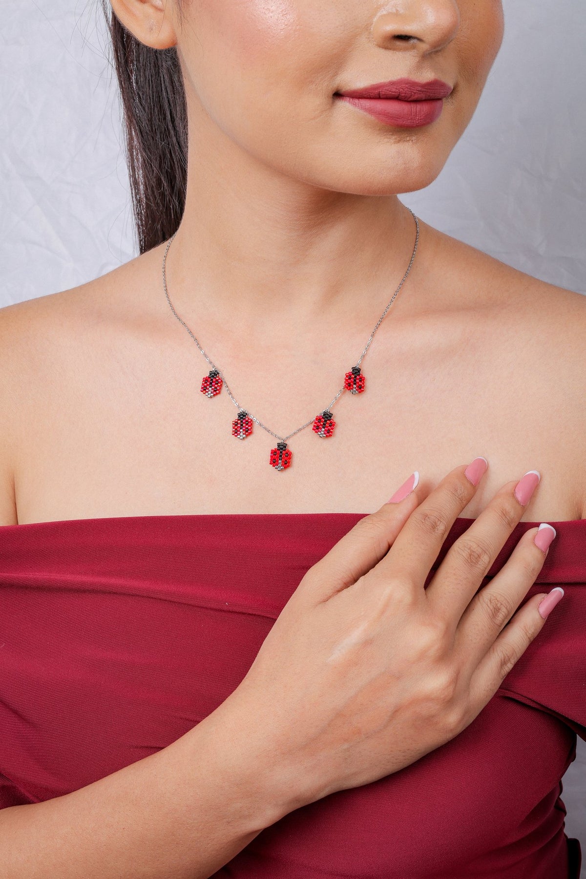 Silver-tone chain necklace with five red and black beaded ladybug charms on a model