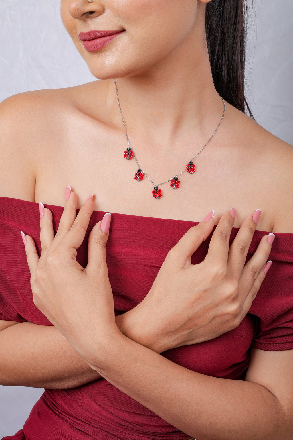 Five red ladybug charms spaced along a fine silver-tone chain, model's arms crossed