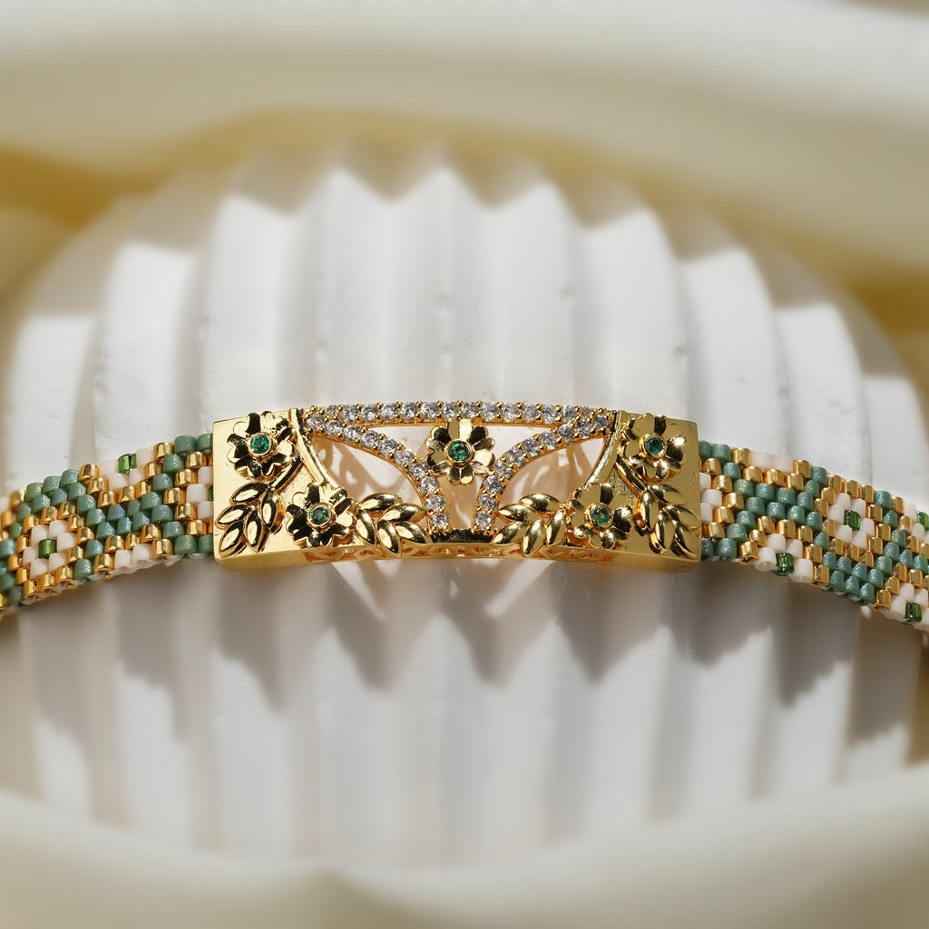 Close-up of gold floral centre plate with green stones and crystal arc on a woven bead band