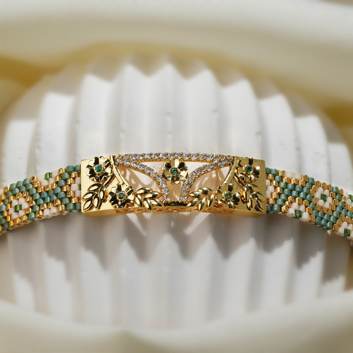 Close-up of gold floral centre plate with green stones and crystal arc on a woven bead band