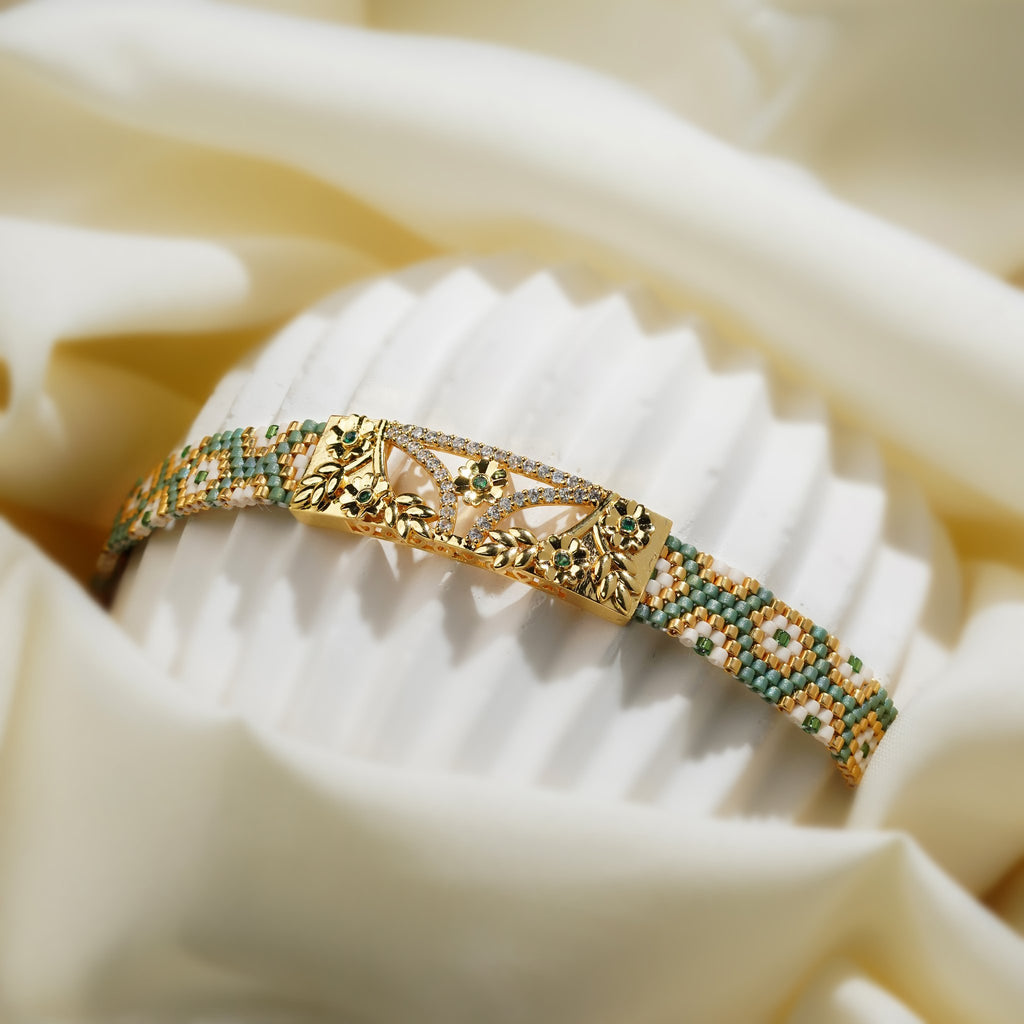 Sage green and gold loom-woven bracelet with filigree plate curved over a fluted white stand