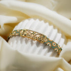 Sage green and gold loom-woven bracelet with filigree plate curved over a fluted white stand