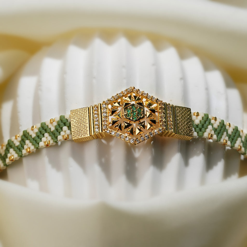Front view of gold hexagon centrepiece with green stones and crystal border on a green woven band