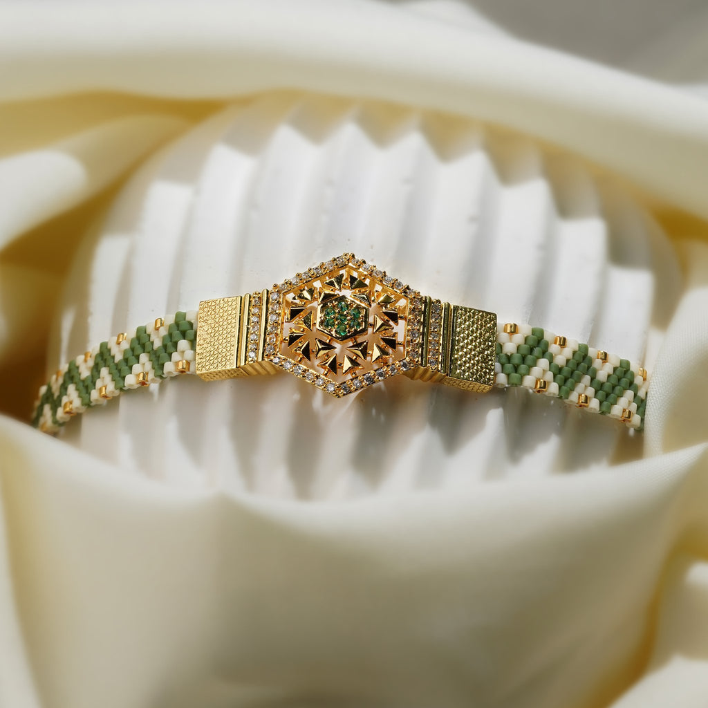 Sage and cream woven bracelet with gold hexagon centrepiece displayed on a ribbed white stand